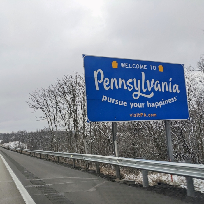 A sign on the side of a highway reading "Welcome to Pennsylvania. Pursue your happiness."